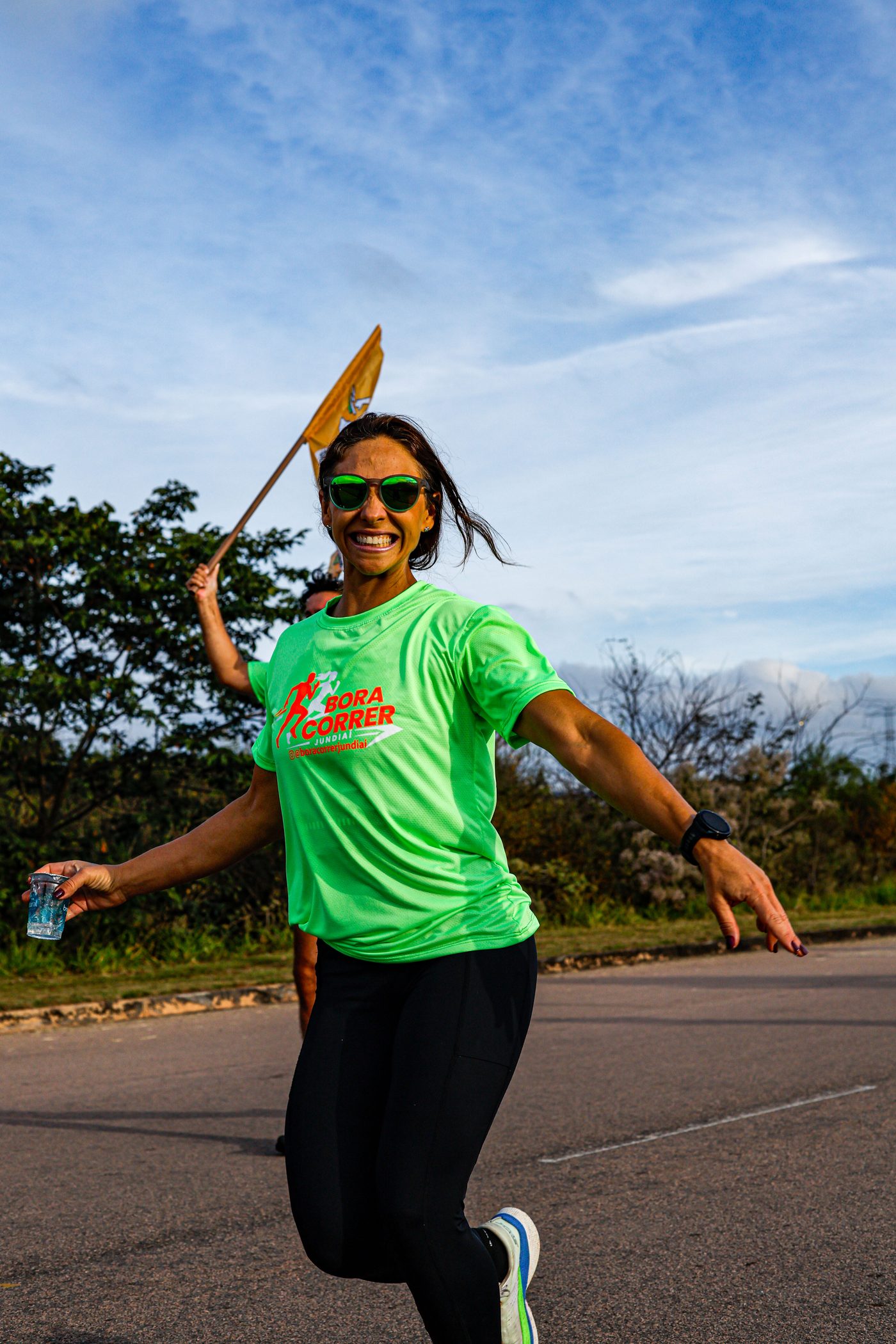 Participante sorrindo e carregando a bandeira do Bora Correr durante o percurso